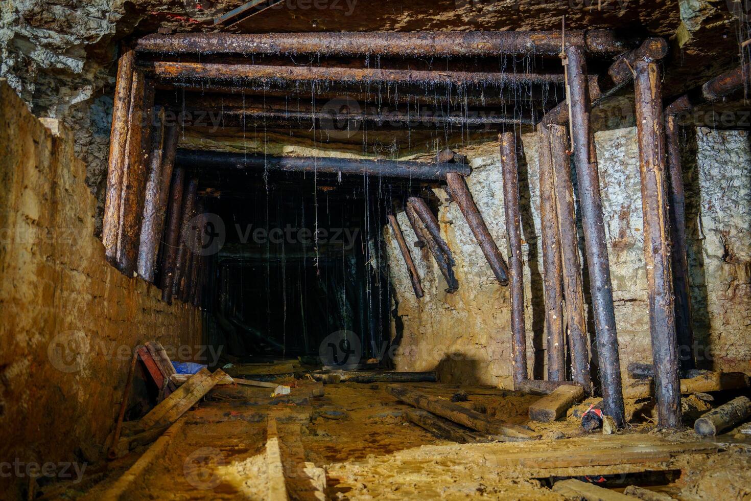 The dark and gloomy abandoned mine tunnel, supported by wooden beams, is filled with debris. Water drips steadily from the ceiling, creating an eerie atmosphere reminiscent of forgotten times. photo