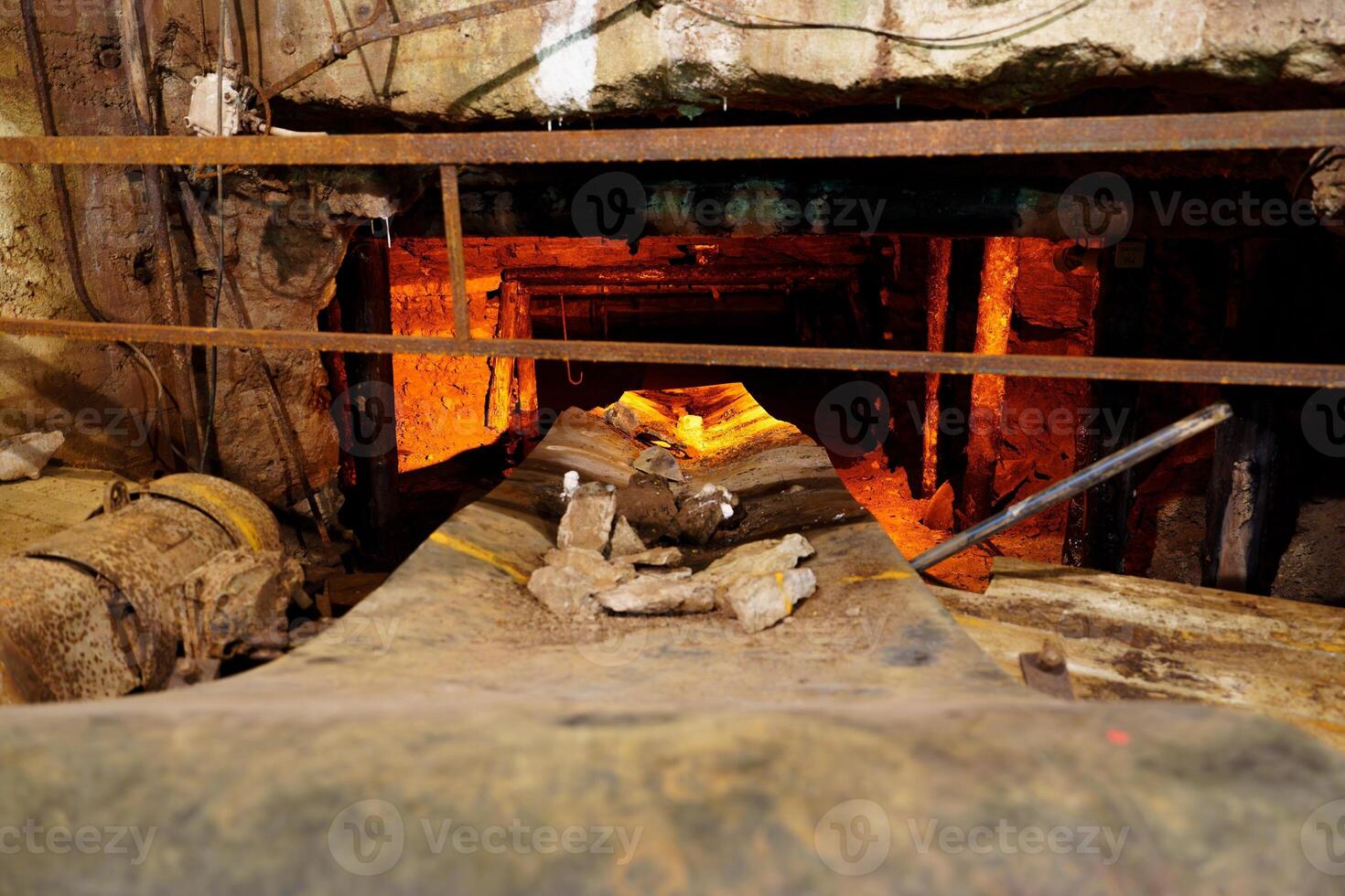 The image depicts a dark factory with a rusty railing and a glowing hot rock on a conveyor belt, surrounded by sparks and flames in an intense industrial atmosphere. photo