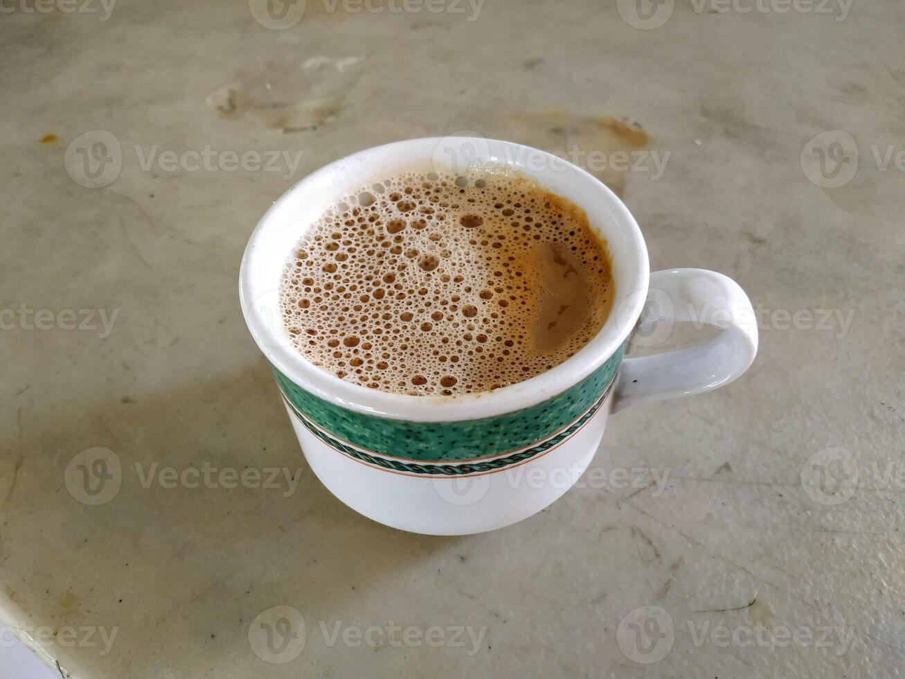 A cup of frothy coffee in a white mug with a green decorative band, placed on a textured surface. photo
