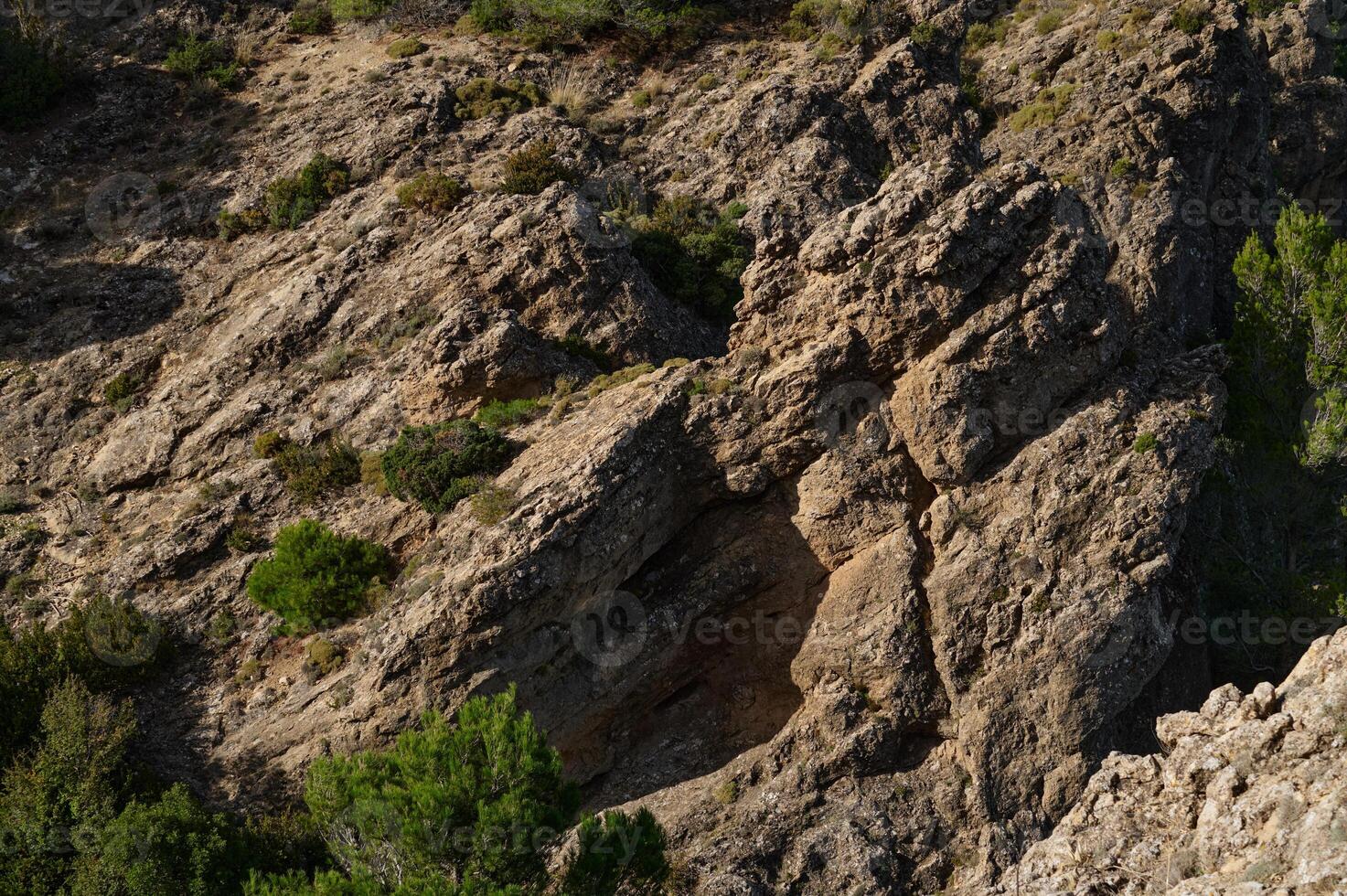 Natural rugged rock formation with green shrubs and bushes photo