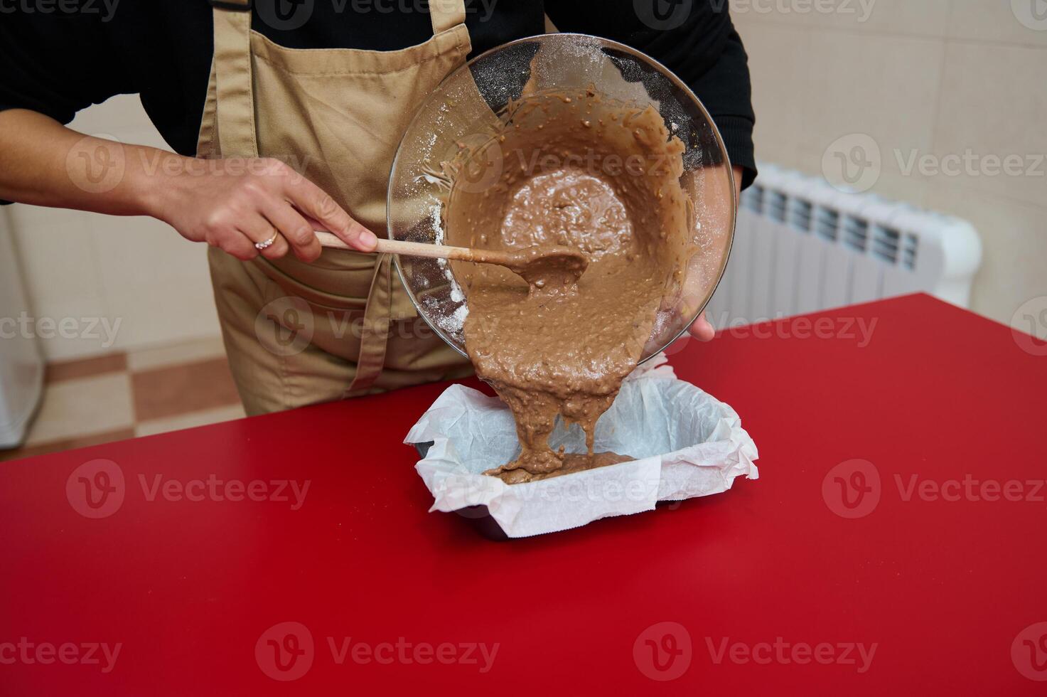 Person pouring cake batter into a baking tray on red surface photo