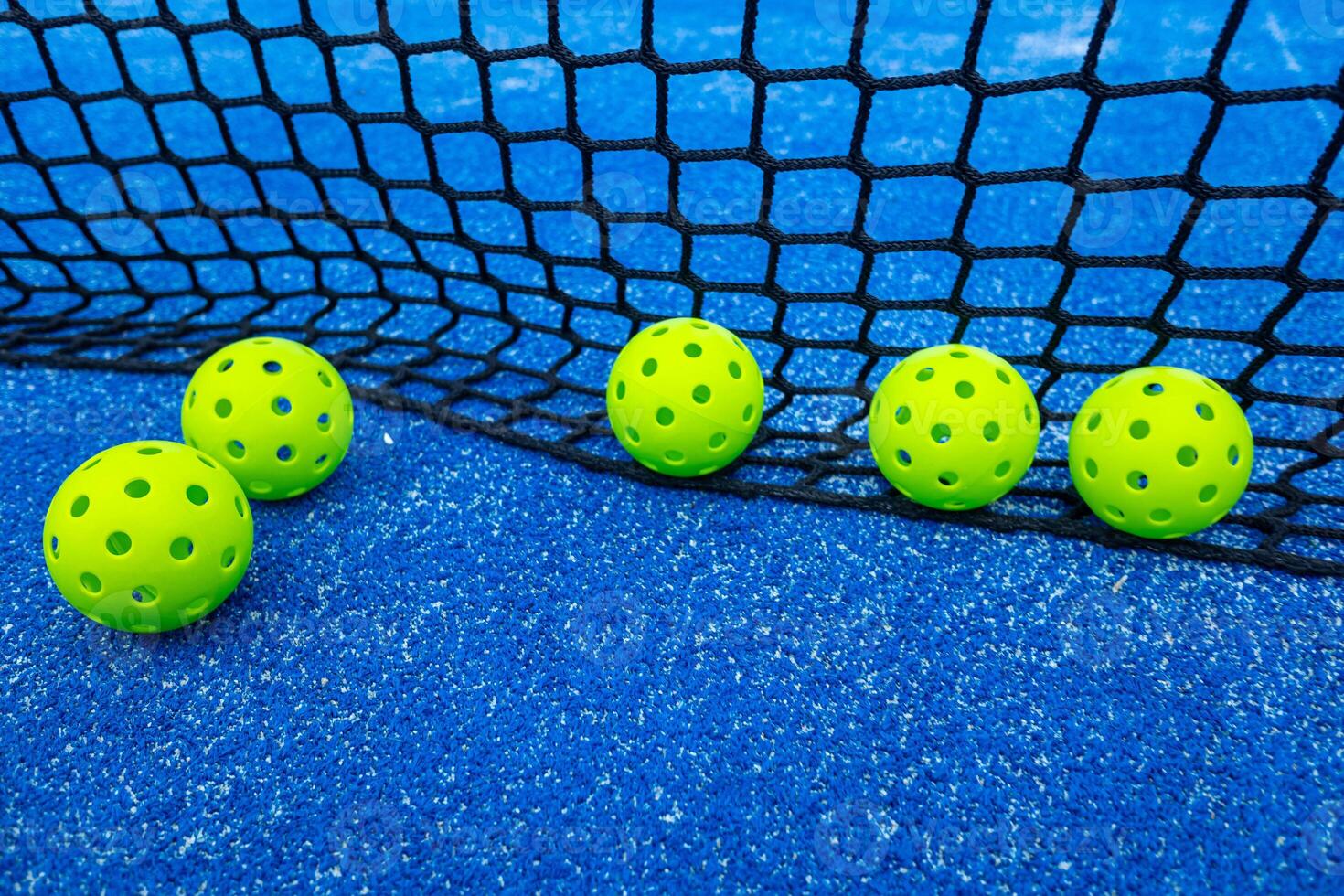 Five balls of pickleball in front of the net, racket sports photo
