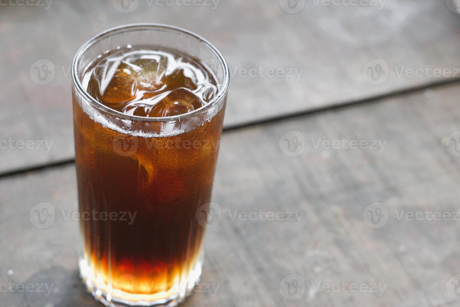 A glass of iced tea with ice cube on wooden table photo