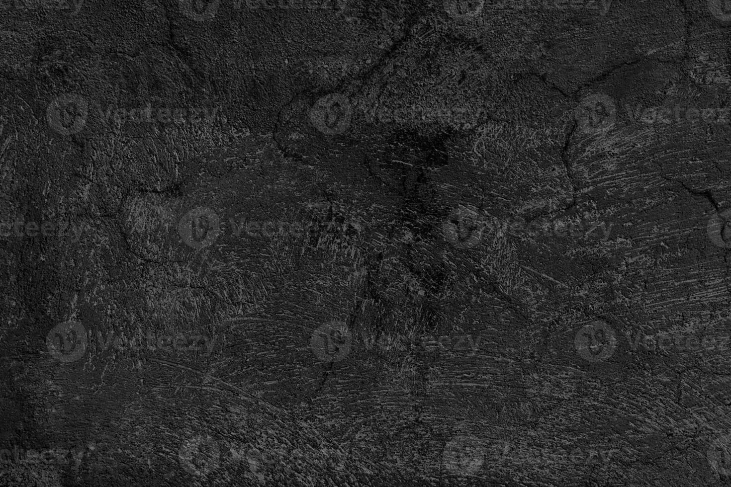 Dark, textured surface that appears to be a close-up of a rough, black concrete or asphalt material. The surface has visible cracks and irregular patterns, giving it a rugged and worn appearance. photo