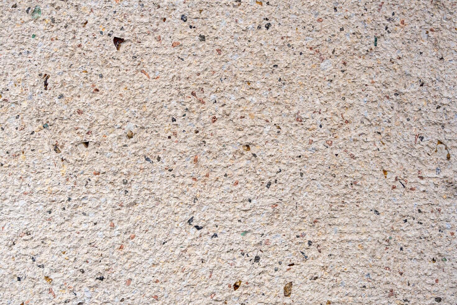 Close-up of a textured surface, likely concrete or a wall, with specks of black, brown, and red. The overall color is light beige or off-white. photo