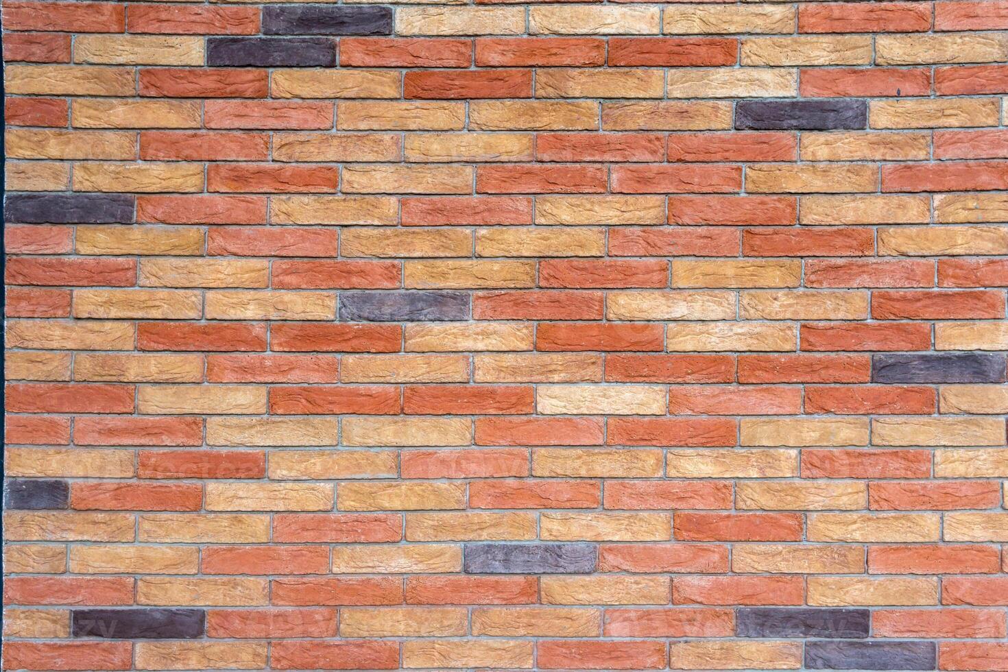 Brick wall with bricks in various colors, primarily in shades of red, orange, and beige, with some darker, almost black bricks. photo