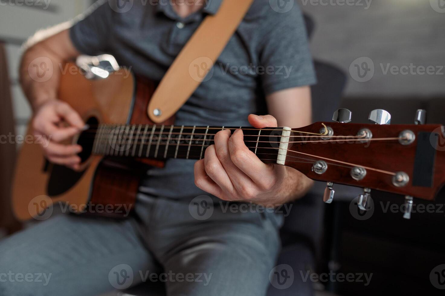 Guitarist paying a acoustic guitar in office. portrait Male musician sitting on sofa and playing music instrument photo