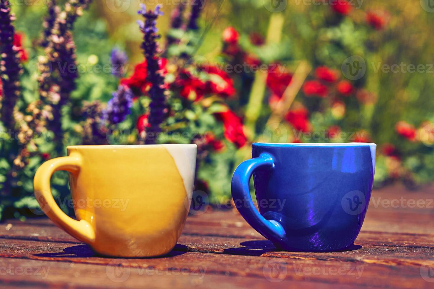 Tea time. Coffee break. Blue yellow cups on wooden in blooming garden photo