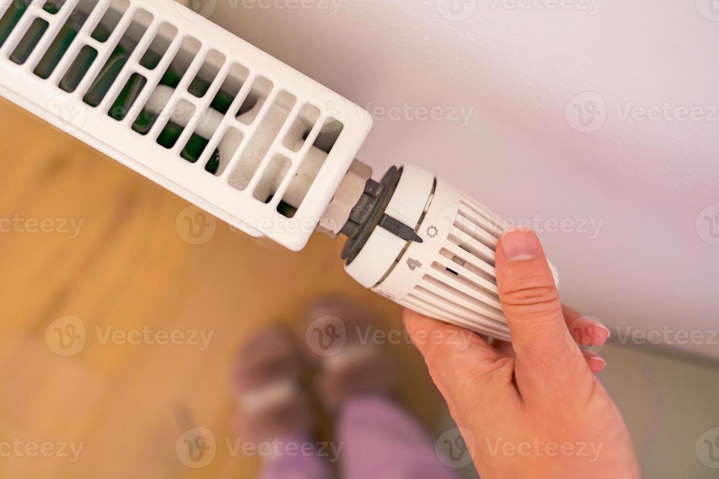 A hand adjusts the temperature on a radiator thermostat, marking the start of the heating season. photo