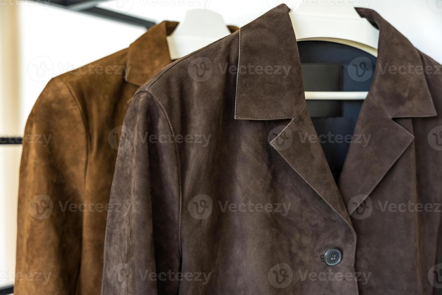 Two brown natural suede jackets of different shades hanging on a hanger on a white background. photo
