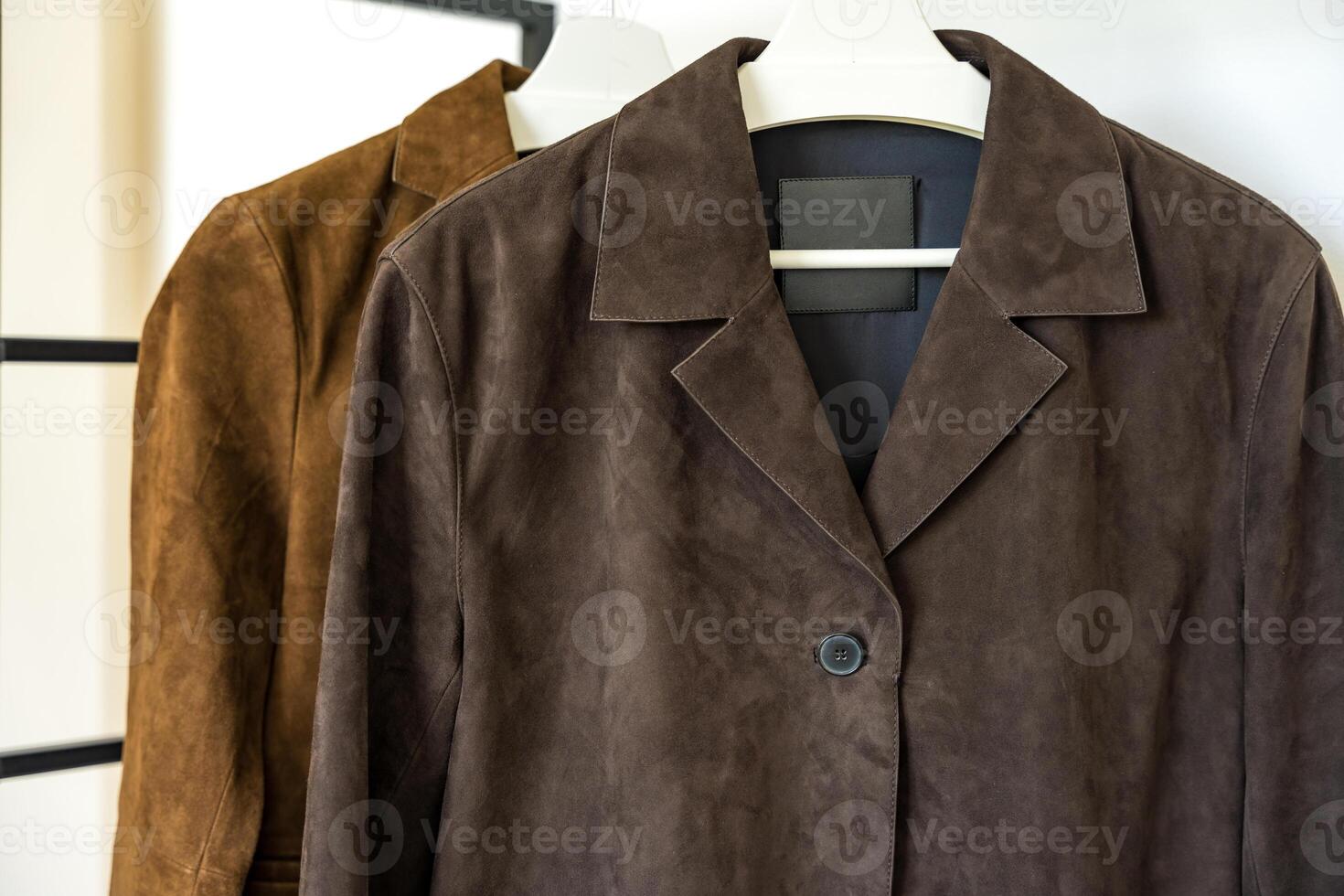 Close up of two brown leather suede jackets of different shades hanging on a hanger at wardrobe photo