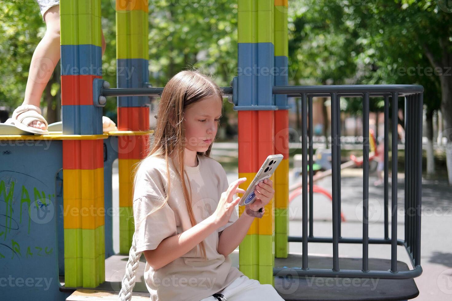 Lonely girl on the children's playground plays on the phone. Smartphone addiction. photo
