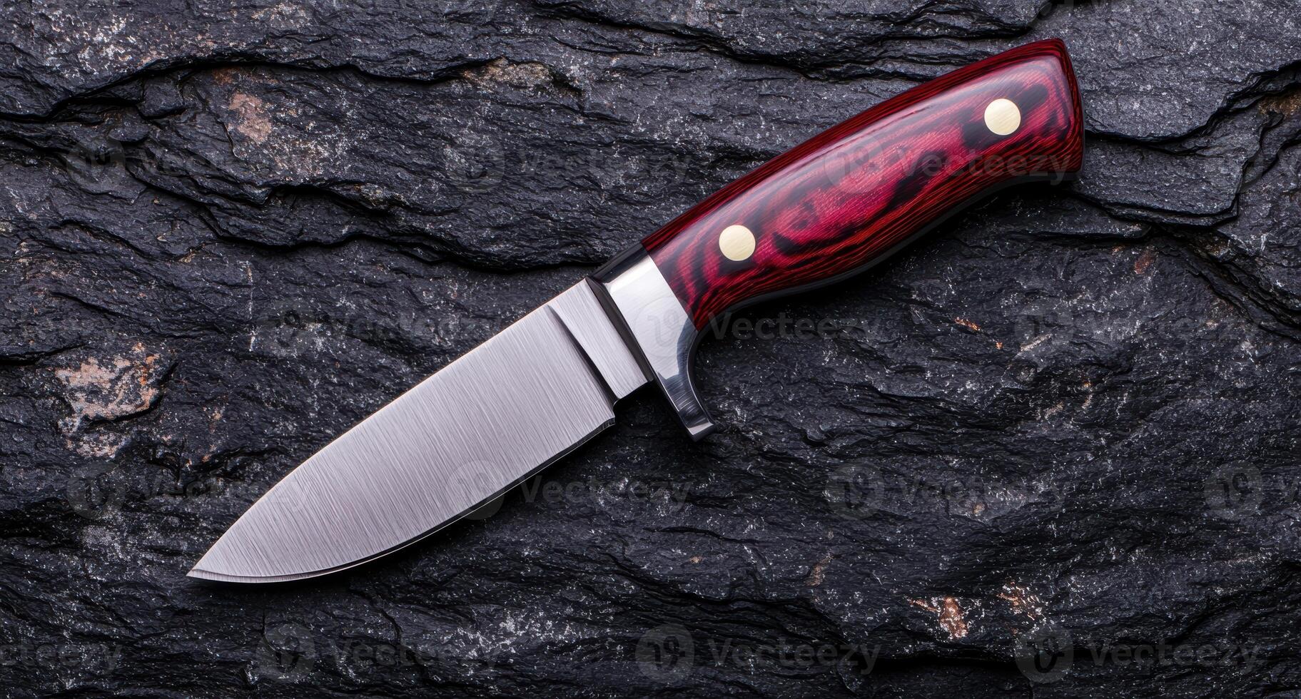 Close up of a sharp hunting knife with a red and black handle on a dark rock background photo
