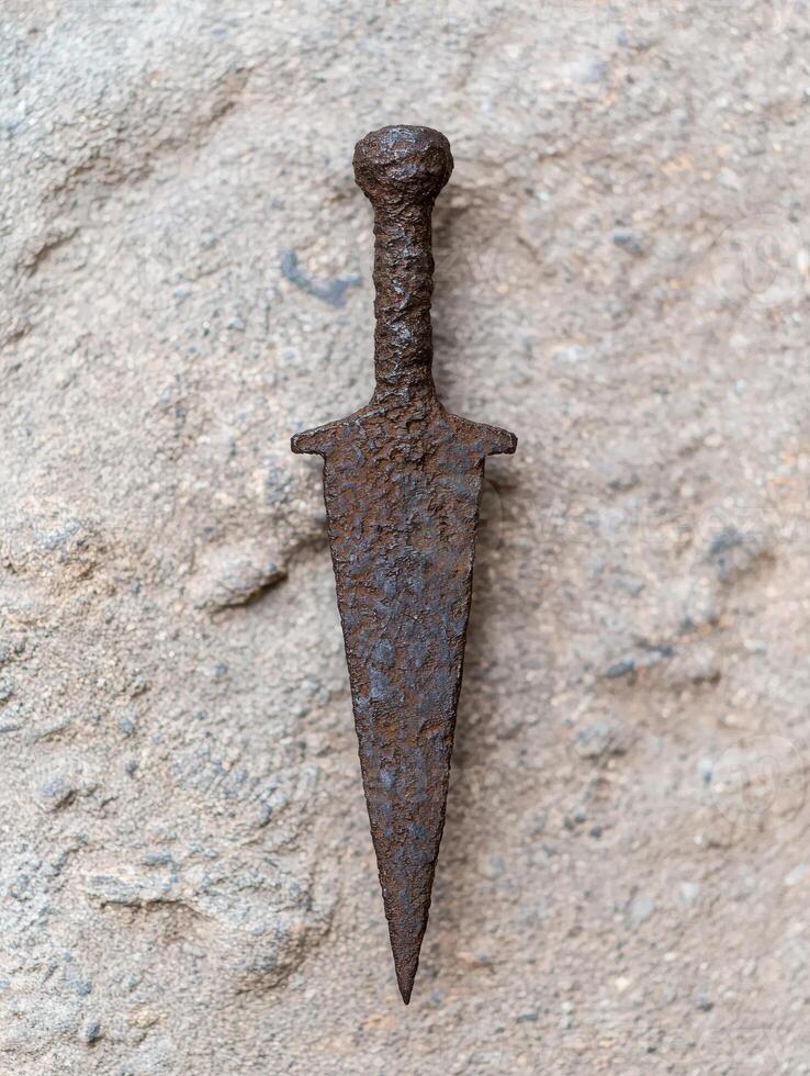Rusted medieval sword on stone surface photo