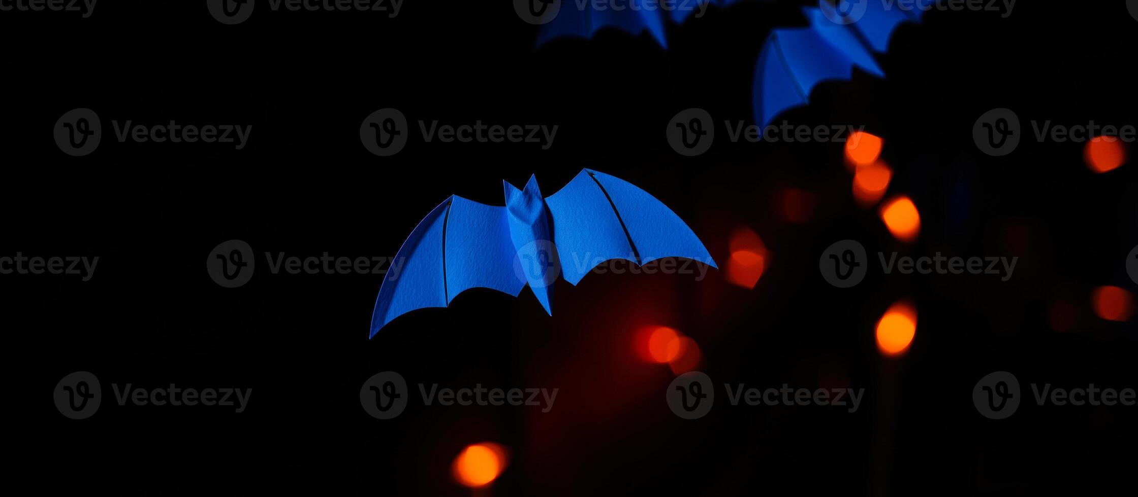 blue paper bat hangs against a blurred background lights photo