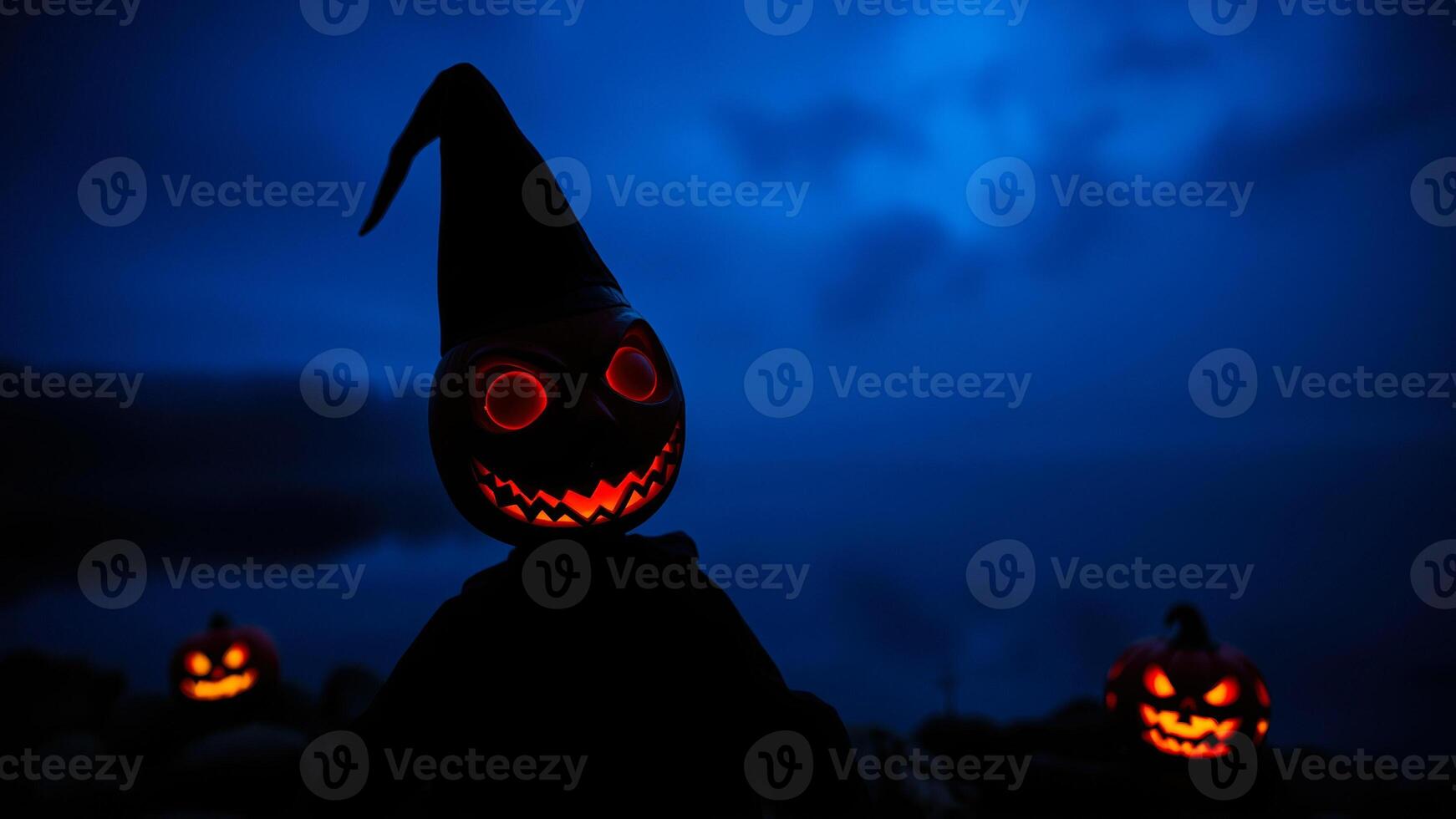 glowing jack-o-lantern with a pointed hat stands against a dark blue sky photo