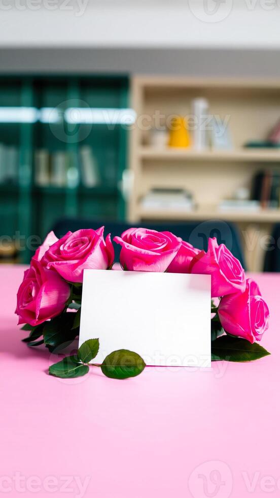 blank card resting on a pink surface surrounded by bright pink roses photo