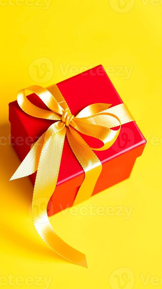 red gift box with a golden bow on a yellow background photo