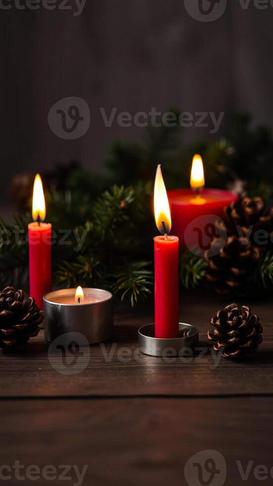 three red candles on a wooden surface with evergreen branches pine cones photo