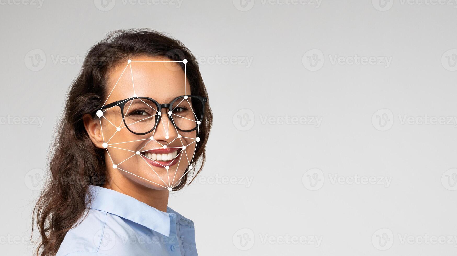 A woman with glasses is smiling while technology captures her facial features. She is in a well-lit studio, showcasing the advancement in facial recognition capabilities. photo