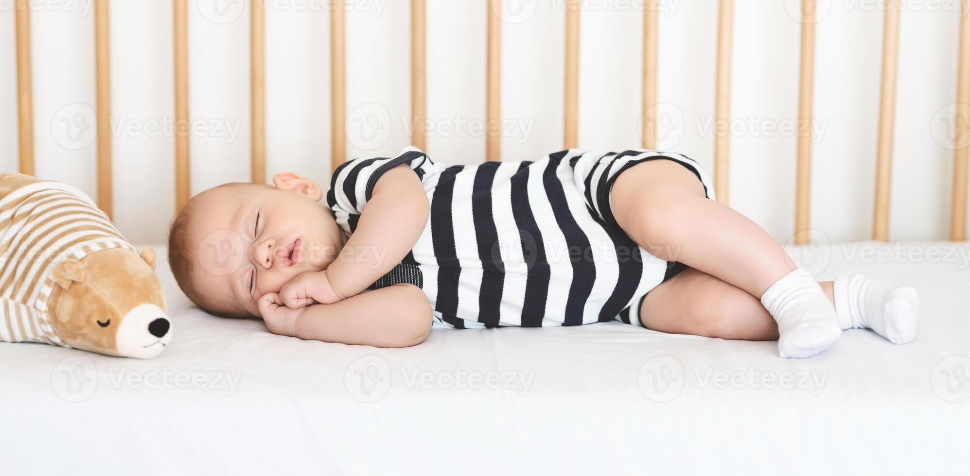 Safe sleeping for babies. Adorable newborn boy napping on his side in crib, clasping hands, panorama photo