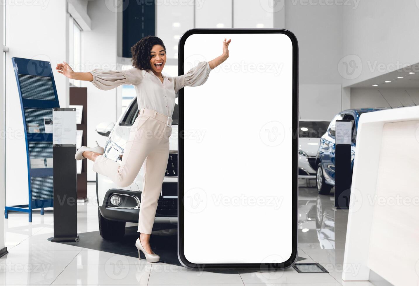 A cheerful salesperson black lady jumps beside a large blank display in a modern car dealership, highlighting cars available for sale while demonstrating enthusiasm for customer engagement. photo