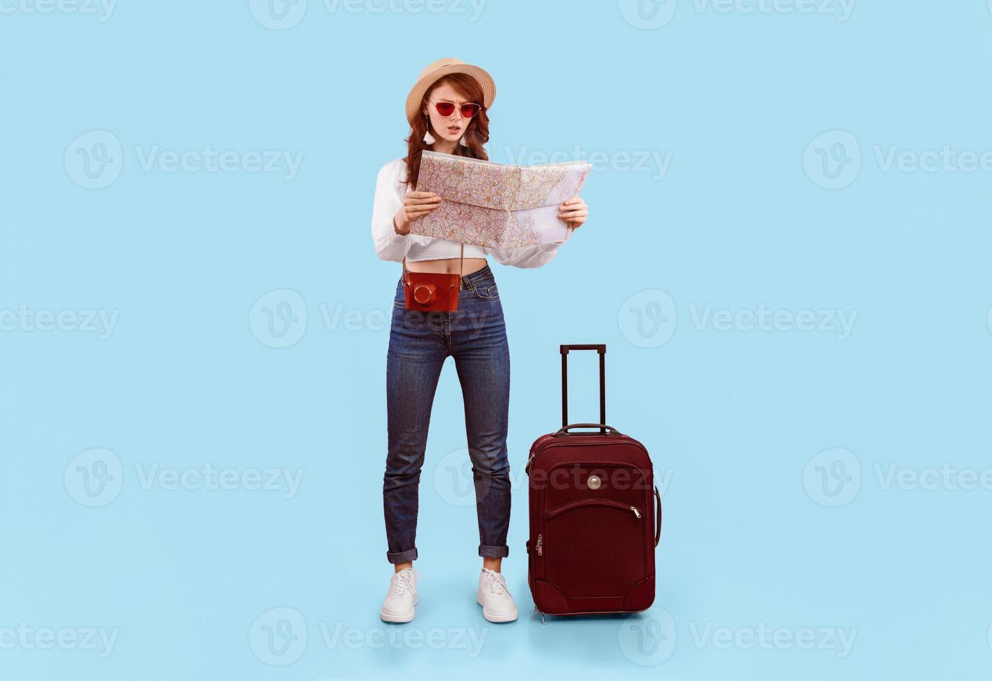 Travel Problem. Shocked Tourist Girl Holding Map Choosing Destination Standing With Suitcase On Pink Studio Background. Vertical photo