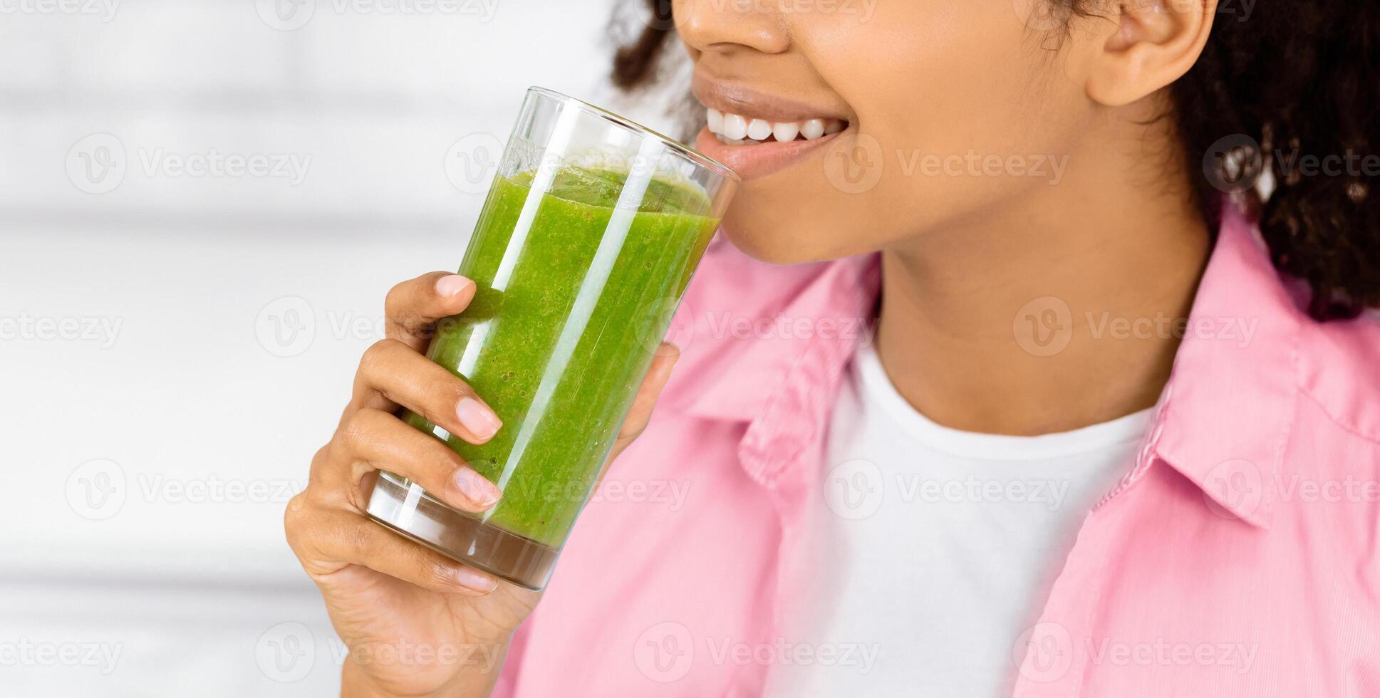 Detox Concept. Close up portrait of black girl holding glass with homemade green juice, looking aside at free space photo