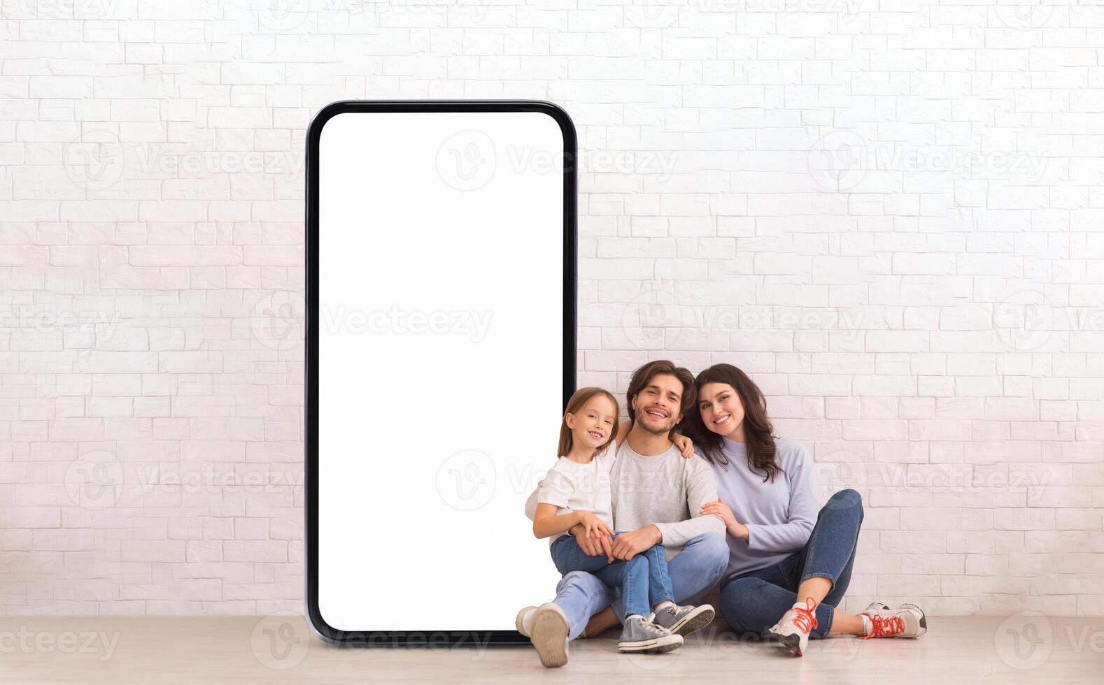 A family of three enjoys quality time together while seated on the floor, framed by a large blank screen. They are smiling and relaxed in a stylish, minimalist environment. photo