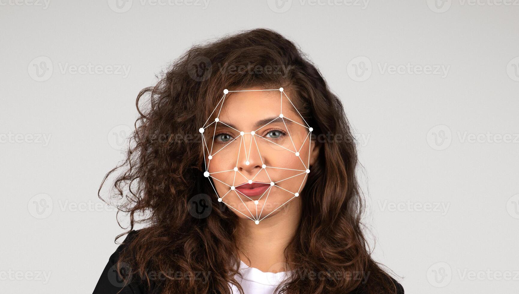 A woman stands against a plain background while facial recognition markers are displayed on her face. She has curly hair and a confident expression as the technology analyzes her features. photo