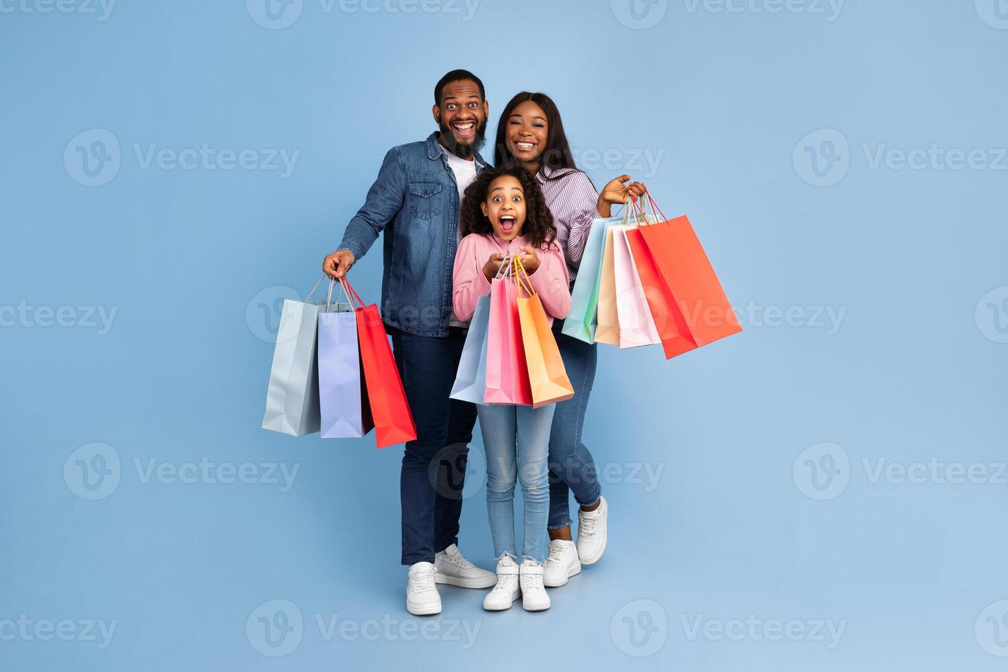 Black Friday Offer Sales And Discounts. Full body length portrait of smiling African American family holding paper bags, feeling happy after successful shopping, isolated on turquoise blue studio wall photo