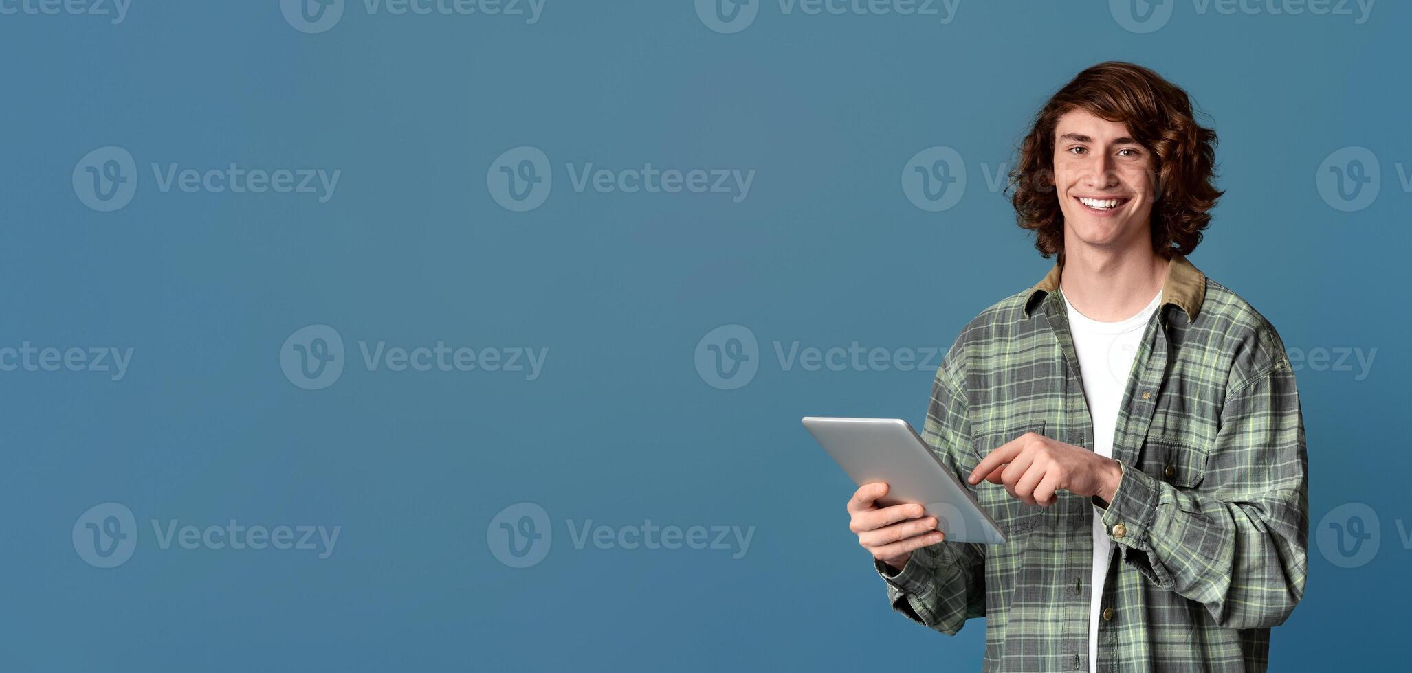 Communicating online. Portrait of young hipster using tablet computer on color background photo