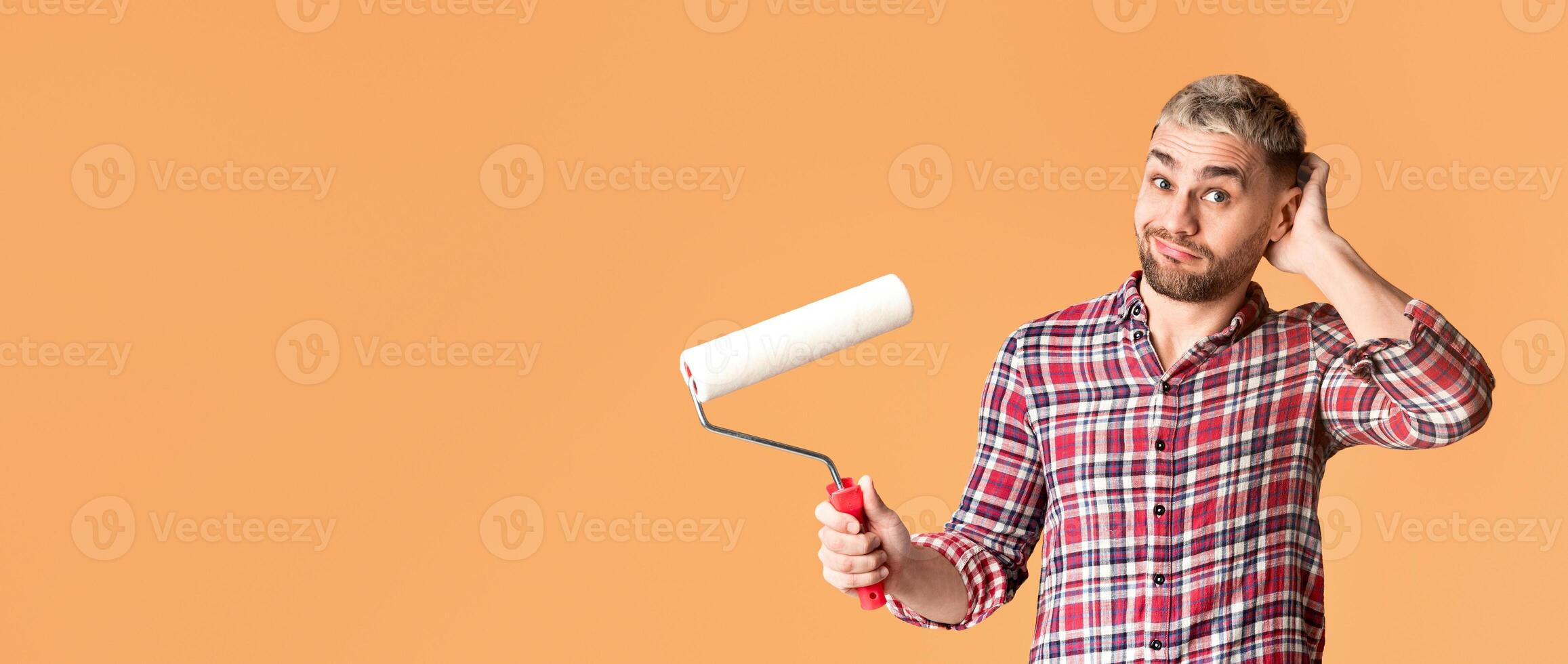 Pensive man scratching his nape and holds roller, free space photo