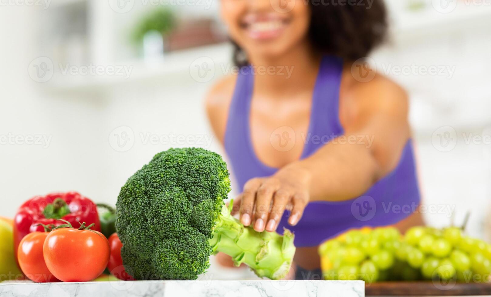 Fit black girl preparing healthy dinner in modern kitchen, taking broccoli, selective focus on vegetables, copyspace photo