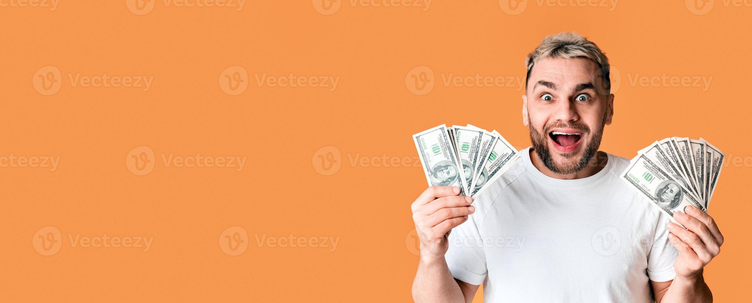 Joyful guy holds a lot of money in his hands on yellow background, empty space photo