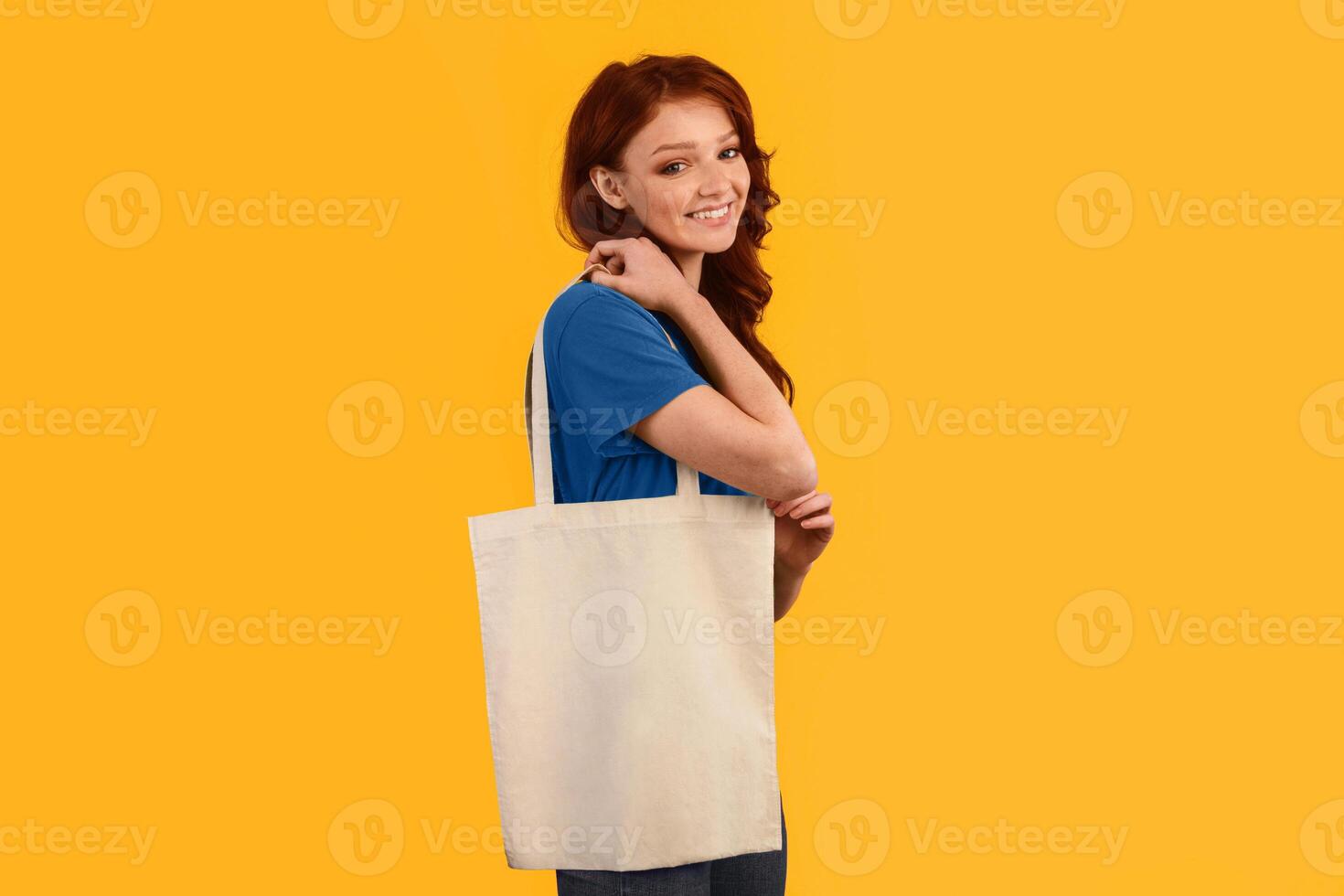 Stop Using Plastic. Smiling Girl Holding Blank Flax Tote Bag Standing Over Yellow Background. Studio Shot, Free Space photo