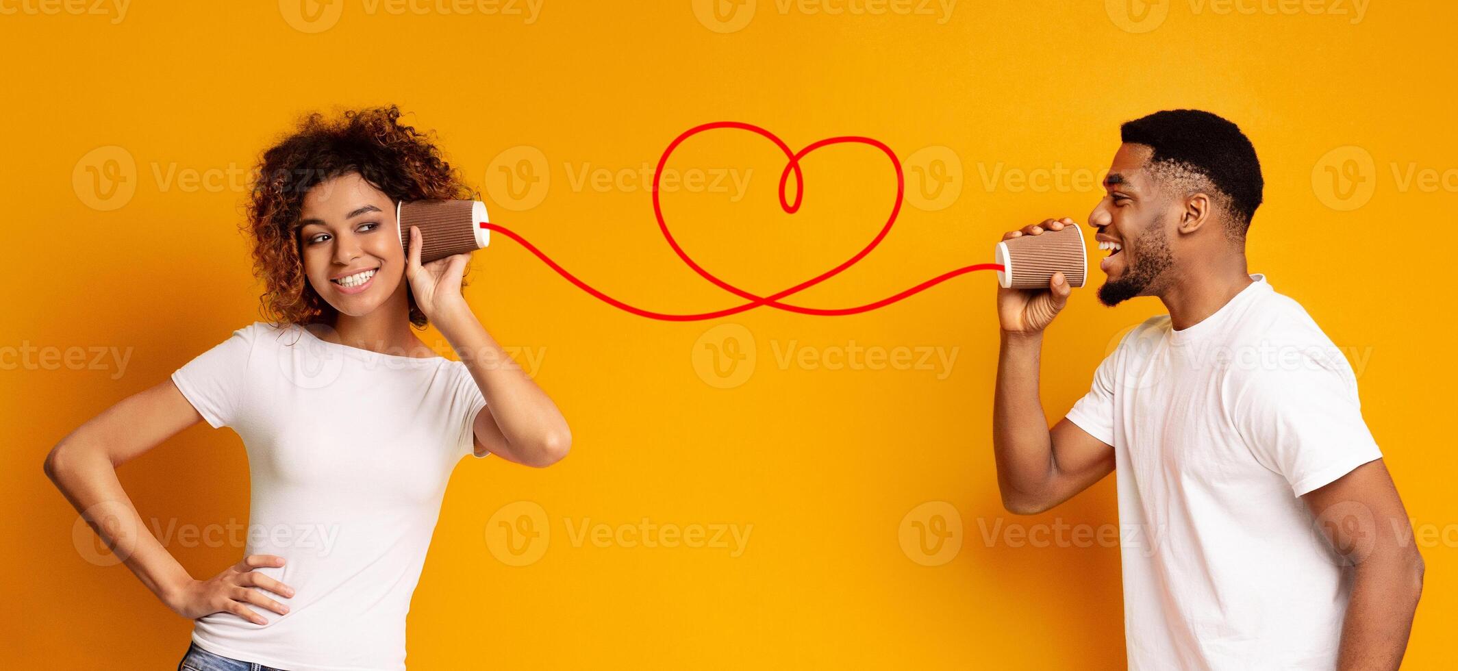 Love message. Lovely african-american couple talking on a tin phone, orange background, panorama photo