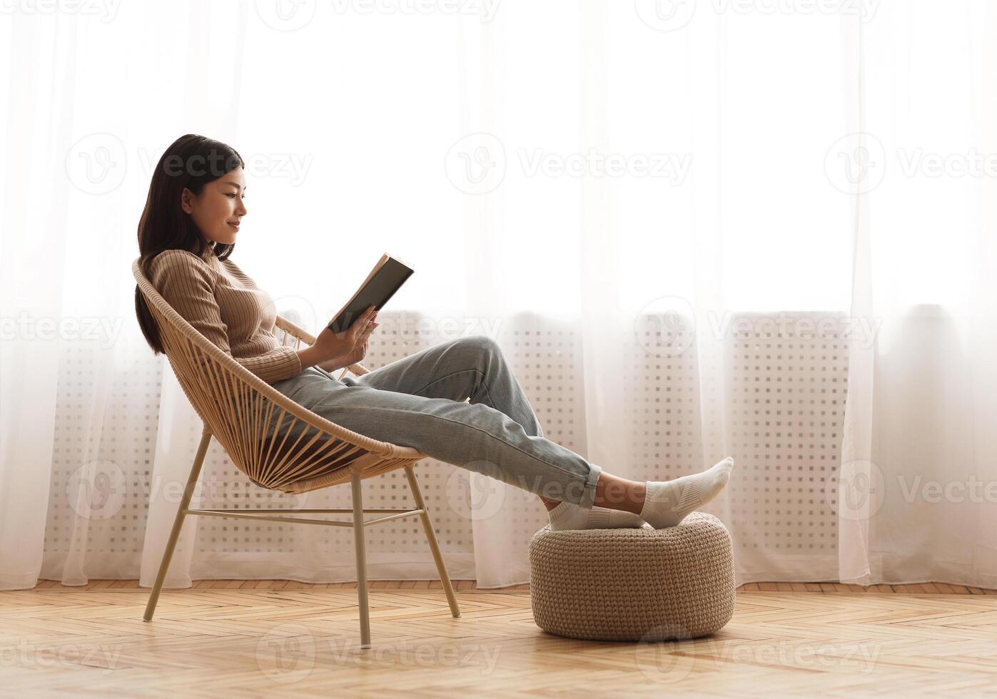 Relaxed girl reading book sitting in chair by the window, enjoying weekend, free space, side view photo