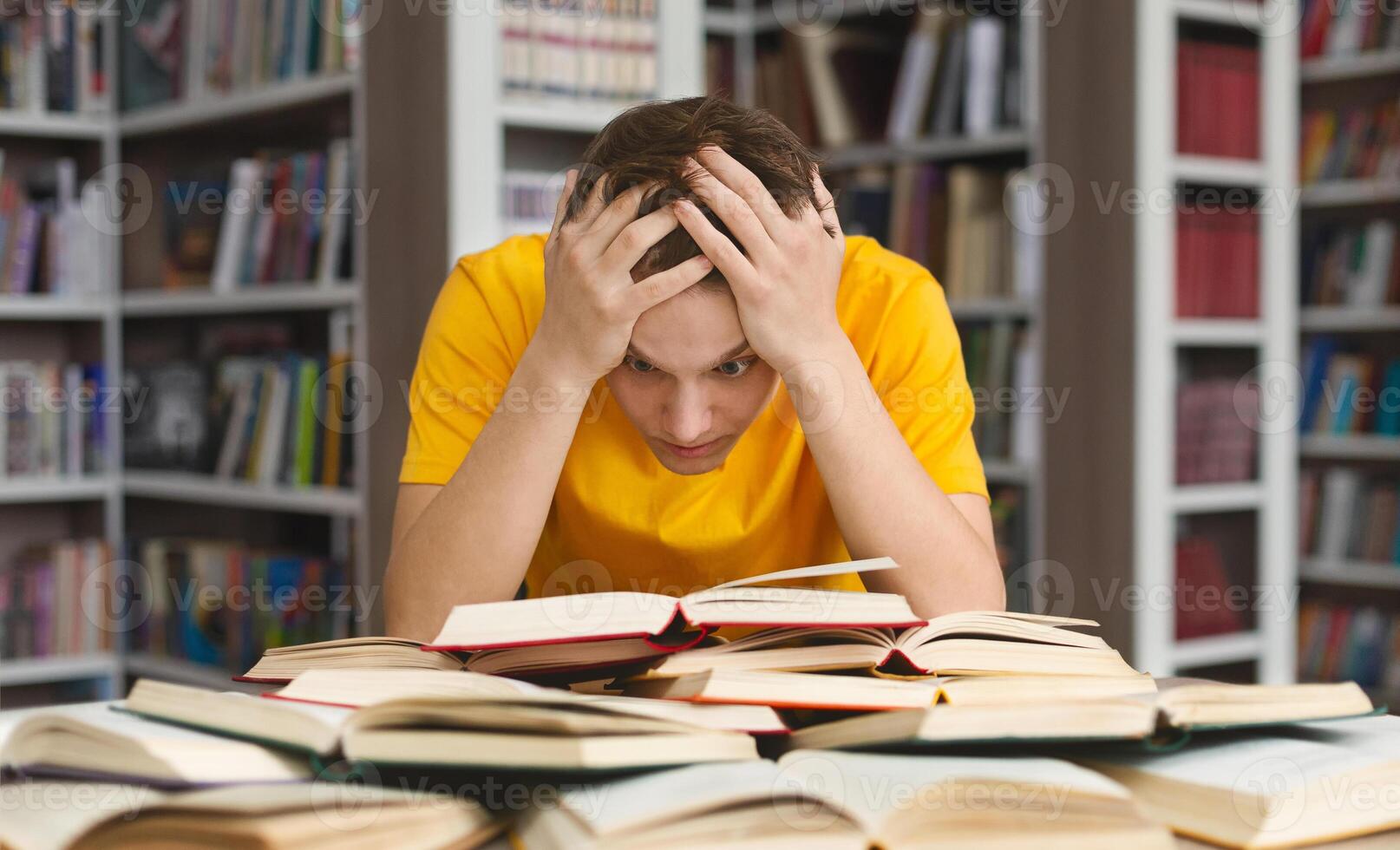 Tired caucasian guy holding head and reading book, getting ready for exams photo