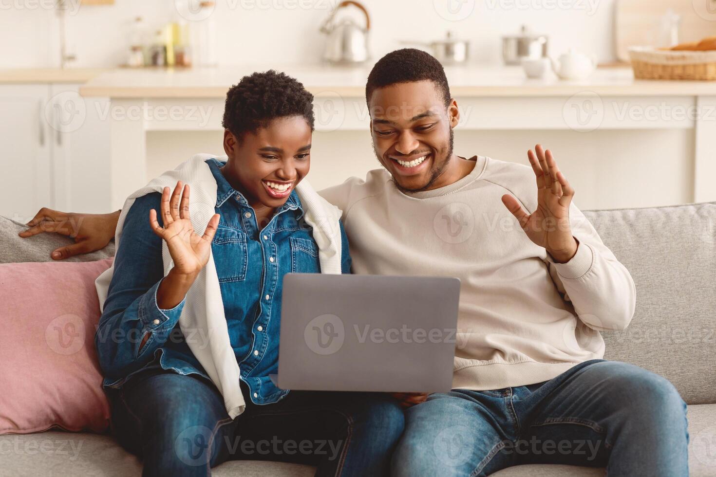 Modern Remote Communication Concept. Portrait of black family of two people making online call with friends during quarantine, using laptop, sitting on couch and talking, waving hands to webcam photo