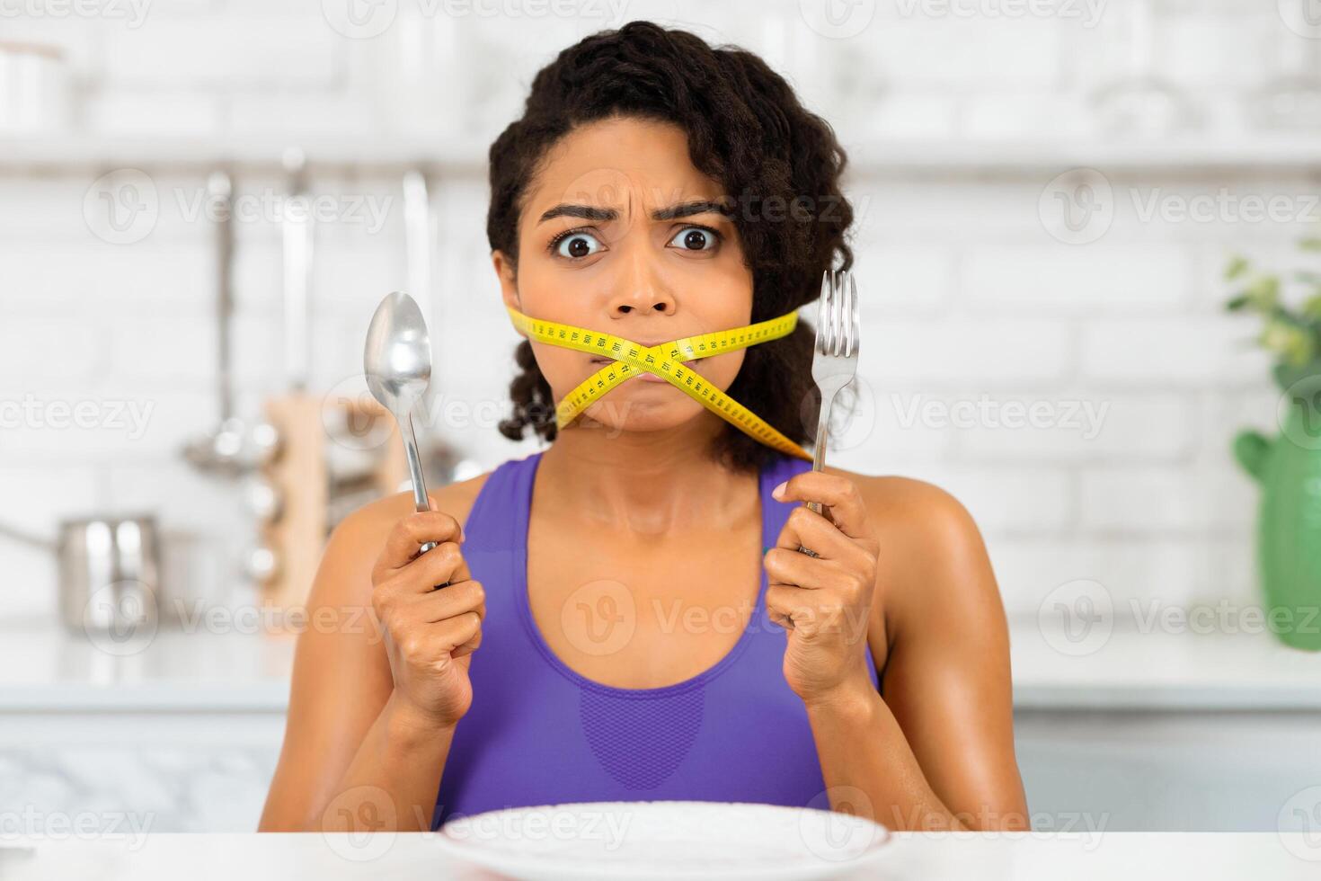 Losing Weight Concept. Close up portrait of african woman with yellow measuring tape around her mouth and wide open eyes photo