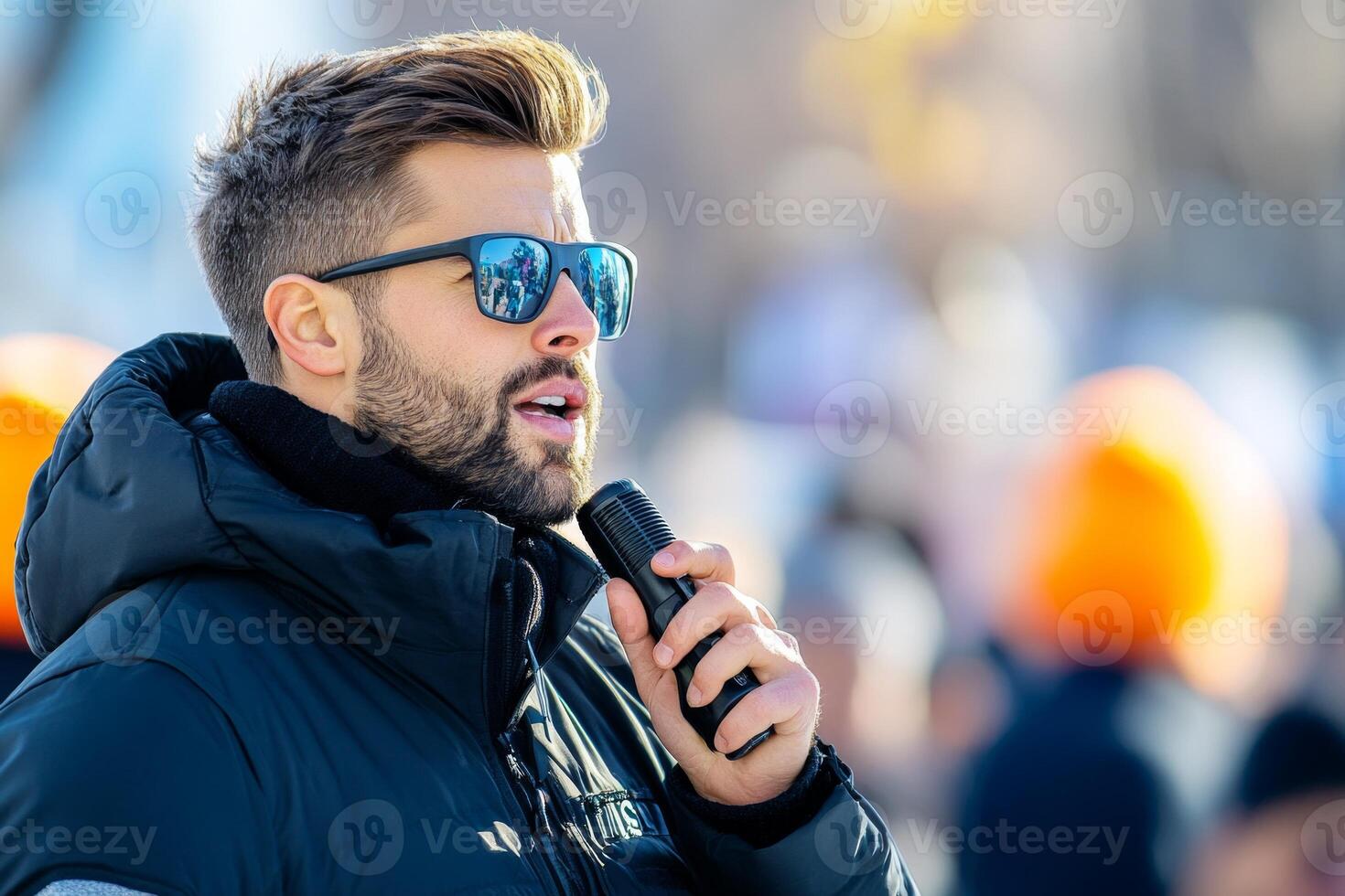 A security professional with sunglasses speaks confidently into a microphone at a public event during daylight photo