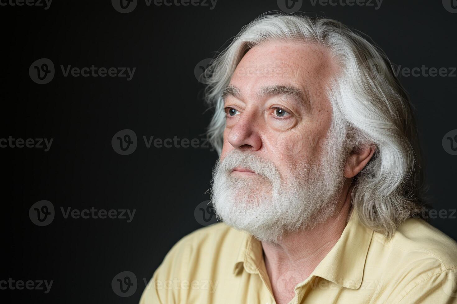 Elderly man with long white hair reflects thoughtfully against a dark architectural background photo