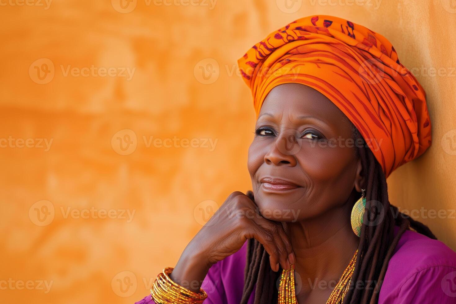An older woman with dreadlocks in an orange head wrap enjoys the warm evening light while resting outside photo
