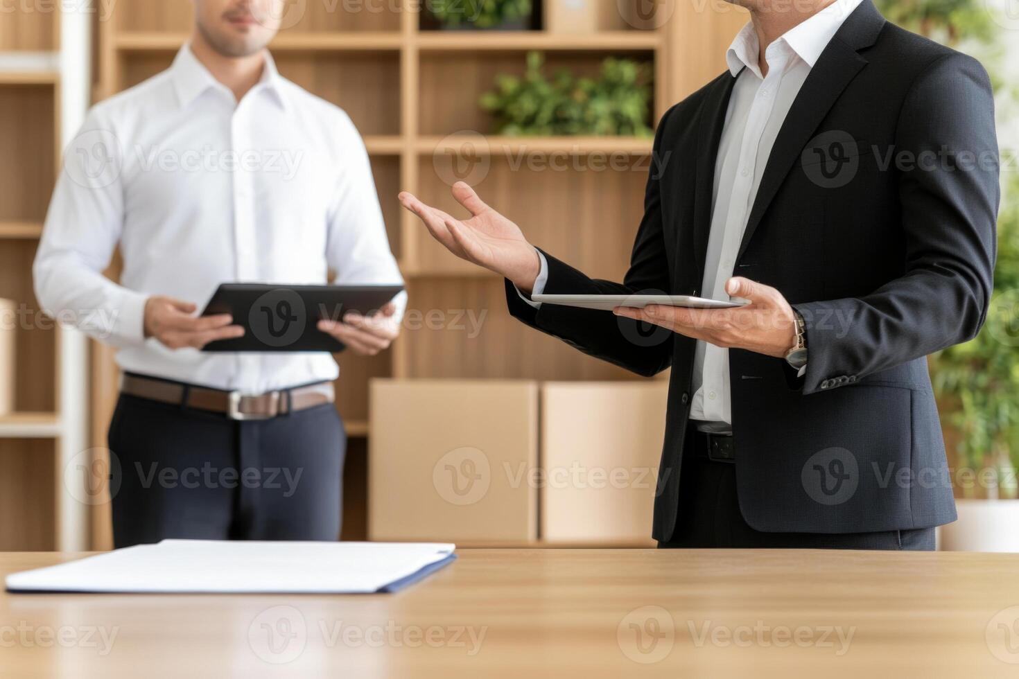 Man gestures during a discussion with a colleague holding a tablet in a modern office environment photo