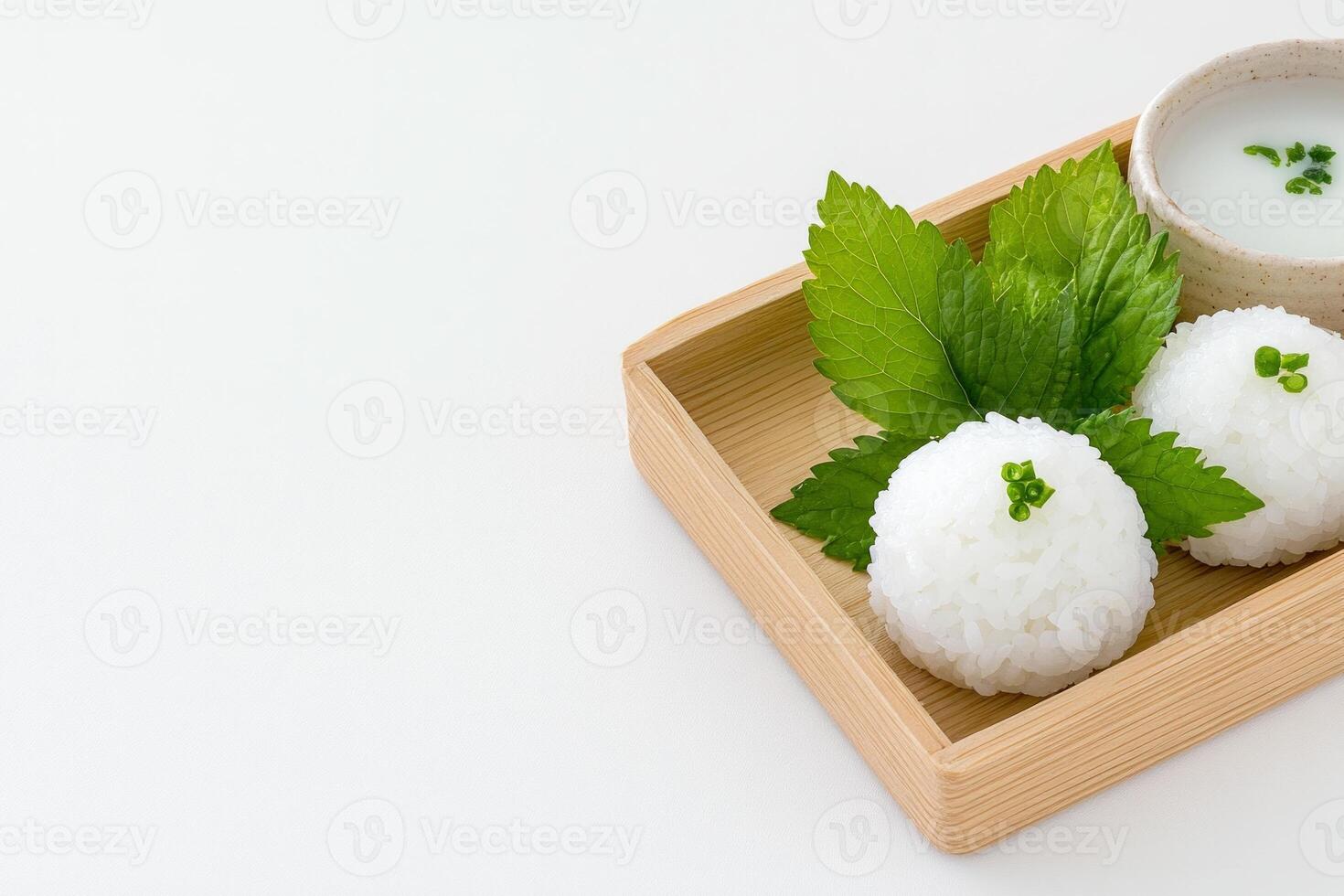 Minimalist presentation of rice balls and shiso leaves on a wooden tray against a clean white background photo
