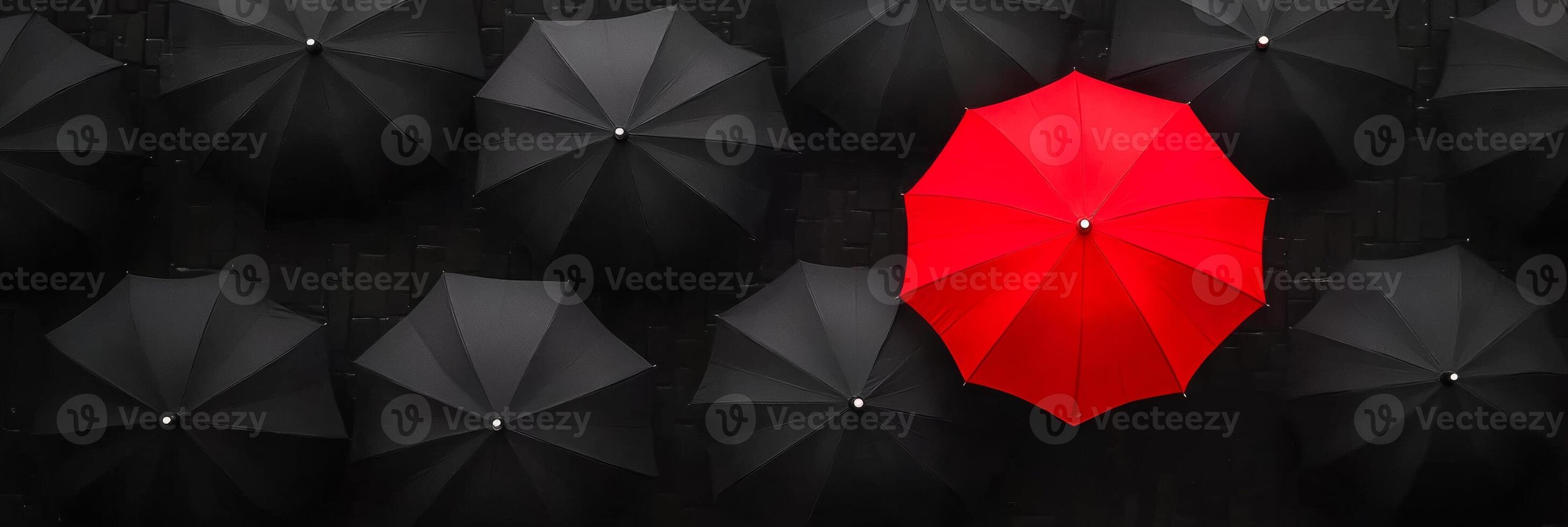 A vibrant red umbrella stands out among a multitude of black umbrellas in a stylish urban setting photo