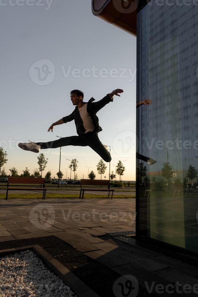 young attractive dancer in casual cloth doing ballet jump on the urban background. Contemporary dance, modern choreography. photo