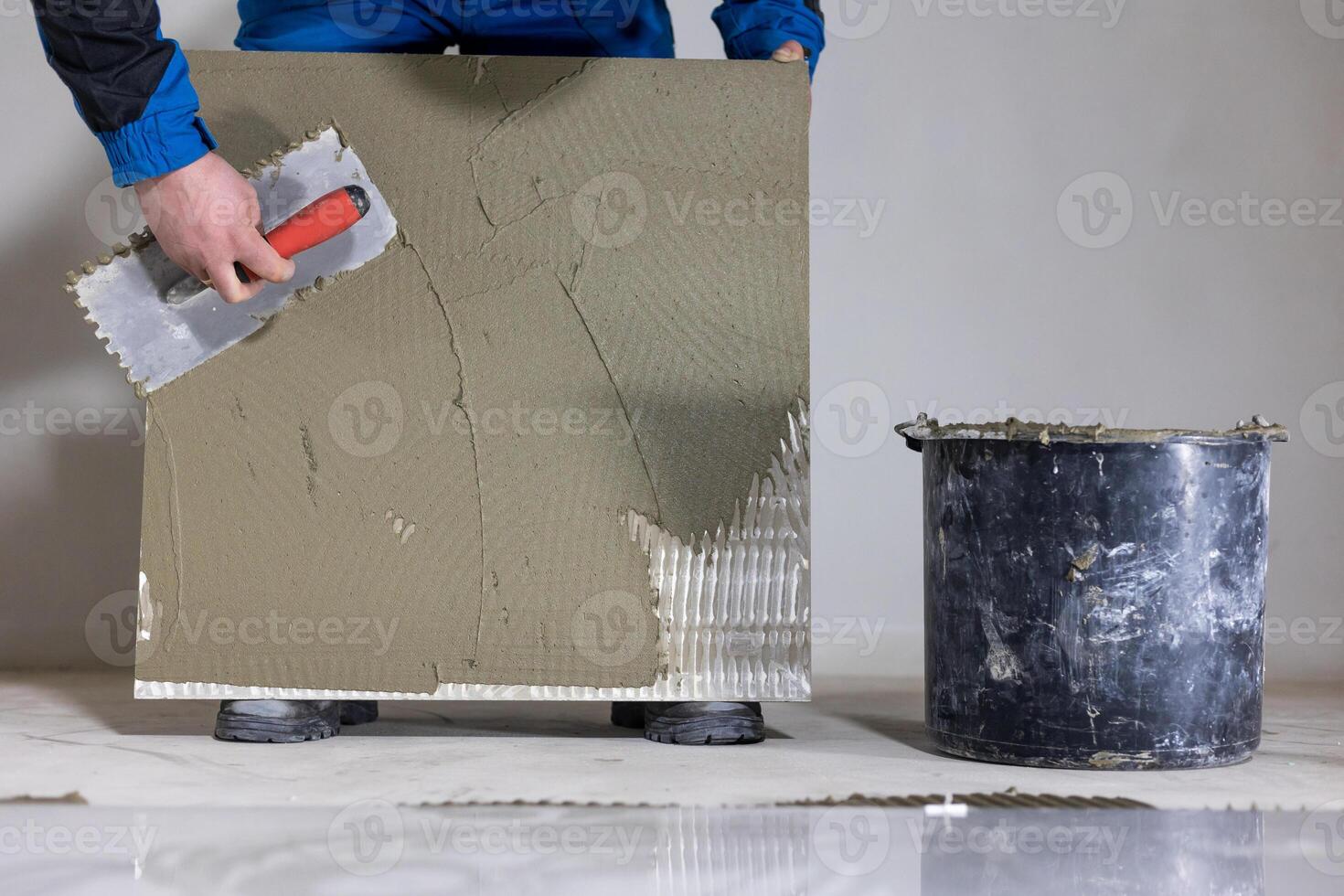 Tiler worker placing or tiling gray ceramic tile in the position over adhesive glue with lash tile leveling system, renovation or recontruction, concept of building photo