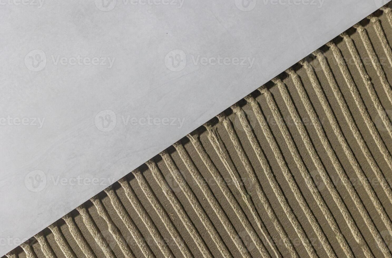 Tiler worker placing or tiling gray ceramic tile in the position over adhesive glue with lash tile leveling system, renovation or recontruction, concept of building photo